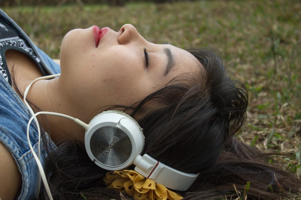 Woman lying in park with her eyes closed listening on headphones