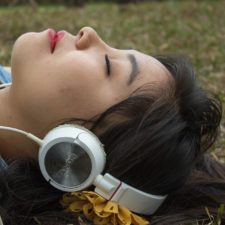 Woman lying in park with her eyes closed listening on headphones