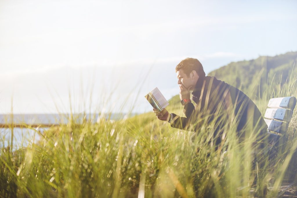 Man on a bench reading, in a field near the edge of a cliff