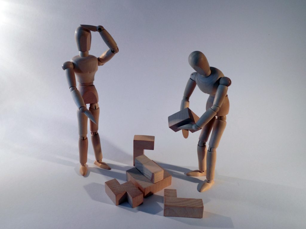 Two wooden men stacking a puzzle
