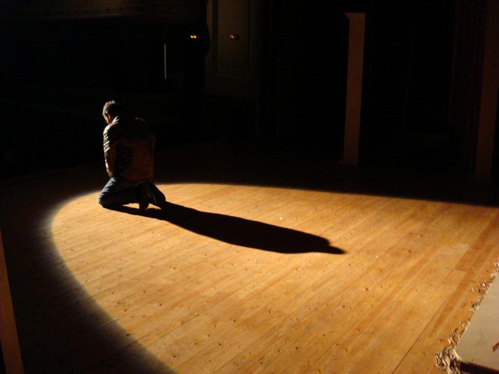 Man on his knees in the spotlight of a stage